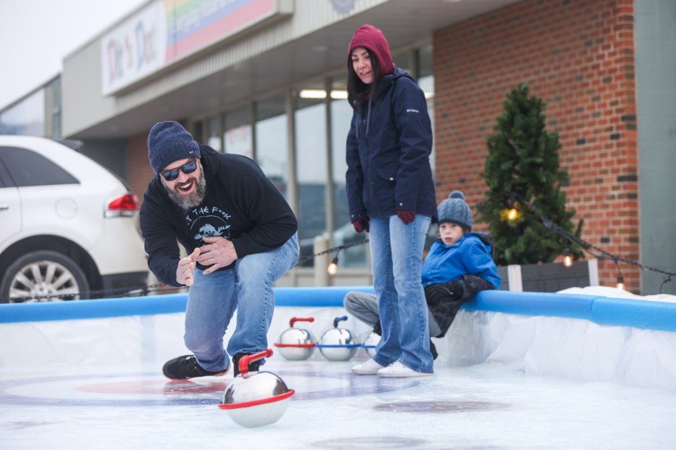 Sean Spence throws a rock on the miniature curling rink constructed by Hub Town Brewing Co. as Pam Gulbrandsen and Mason Ollenberger spectate on Jan. 15.