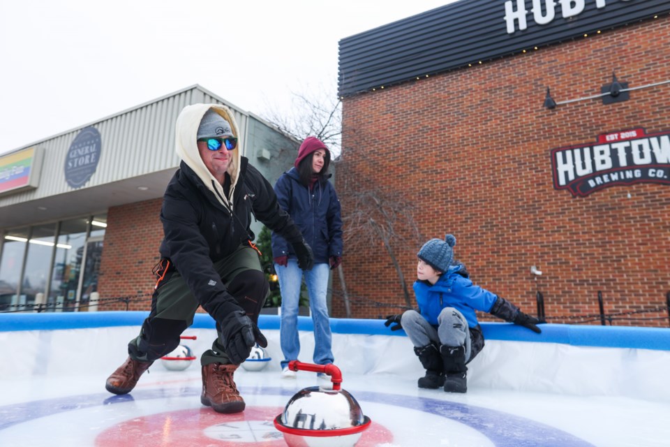 Andrew Gulbrandsen throws a rock on the miniature curling rink constructed by Hub Town Brewing Co. as Pam Gulbrandsen and Mason Ollenberger spectate on Jan. 15.