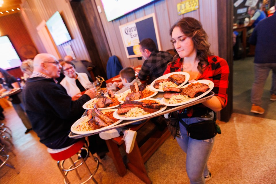 Waiter Trinity Drake doles out plates of BBQ during a fundraiser for the 2023 Alberta Summer Games at Big Sky BBQ on March 2, 2023.