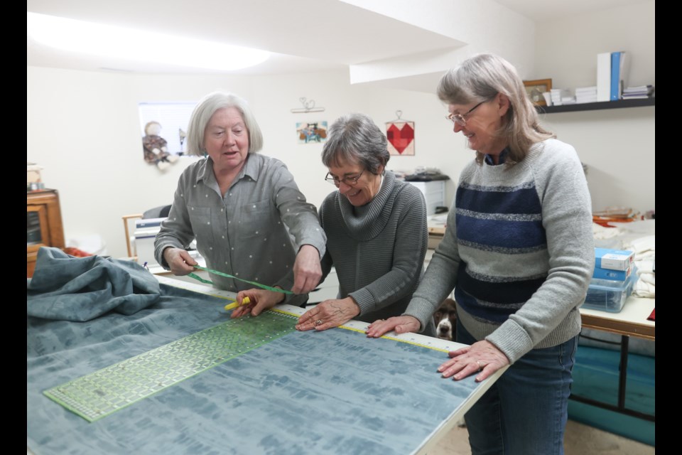 (Left to right) Debra Graham works on quilting material at her home with Jacquie Rhodes and Joanne James on March 11, 2023. The three are members of the Okotoks chapter of Victoria's Quilts, a national volunteer organization that makes quilts for cancer patients.