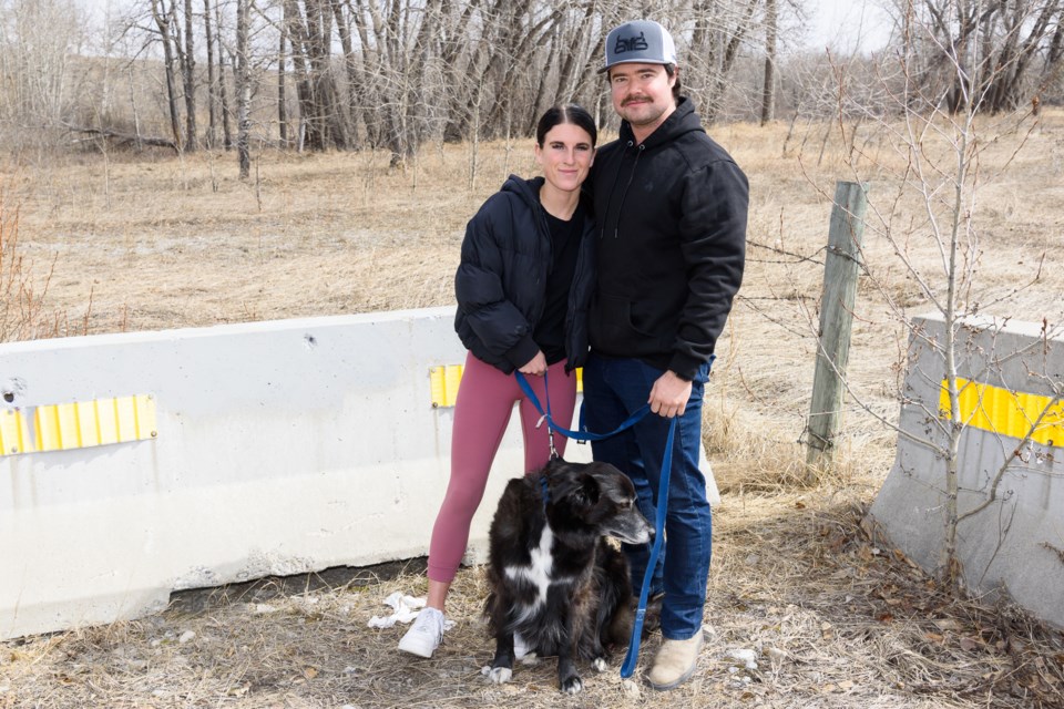 Emily Rawson (left) and Greg Saulnier with Buck, Rawson's border collie cross, stand for a photo on April 18, near the scene of an April 16 incident that saw Buck and Greg stuck in an abandoned septic tank. The incident took place on private land along 370 Ave, east of the Okotoks Dawg's Stadium.