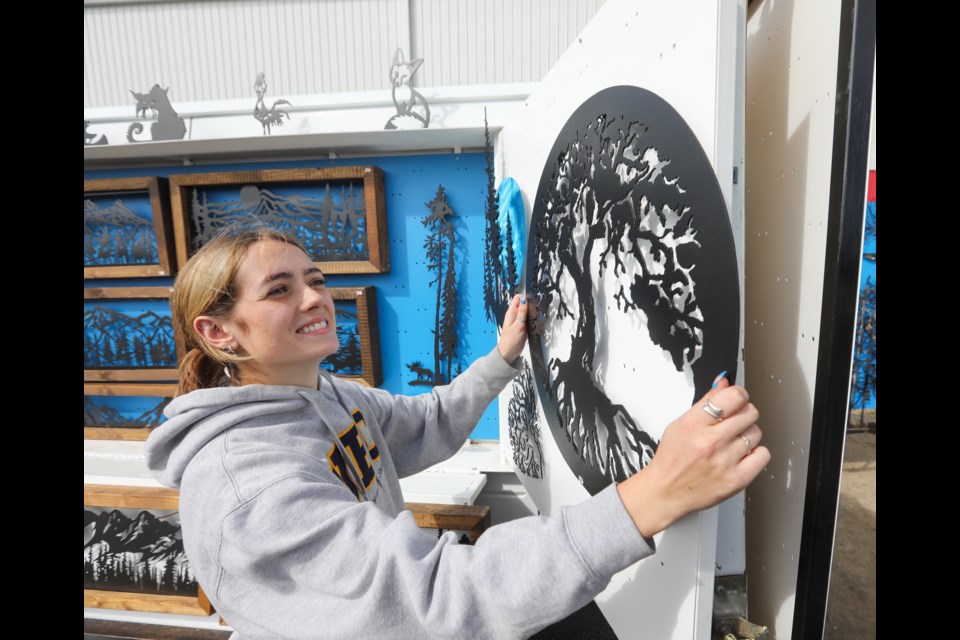 Kiera Sweeney hangs up a piece of metal art on display at Michael Perks' Little Monkey Metalwork stand on opening day of the Millarville Farmers' Market on June 17.