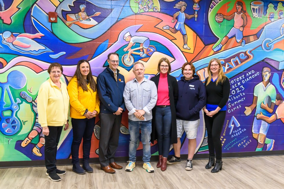 From left to right, Sandi Kennedy, AlbertA Summer Games chair, Okotoks Coun. Rachel Swendseid and Brent Robinson, mural artist Scott Clark, Mayor Tanya Thorn, Coun. Oliver Hallmark, and Games director of culture Karas Wright, at the unveiling of the 2023 Alberta Summer Games legacy mural at the Okotoks Recreation Centre on June 20. 