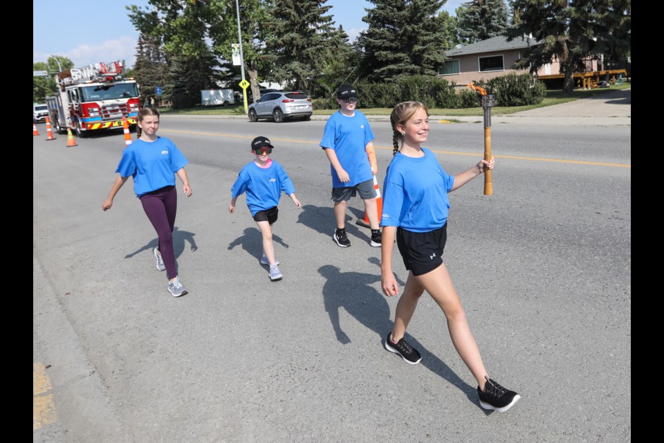 Abby Spicer carries the torch, followed by (from left) Carianne McGregor, Amberly Musgrove, and Carter Musgrove in the Torch Celebration relay to kick off the Alberta Summer Games in Diamond Valley on July 19, 2023. The relay ran from the Oilfields Regional Arena Library up 3 Street West to the town hall.