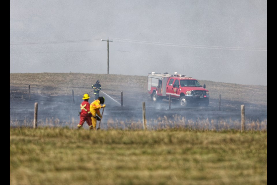 Firefighters work to extinguish a grass fire south of Okotoks on August 6.