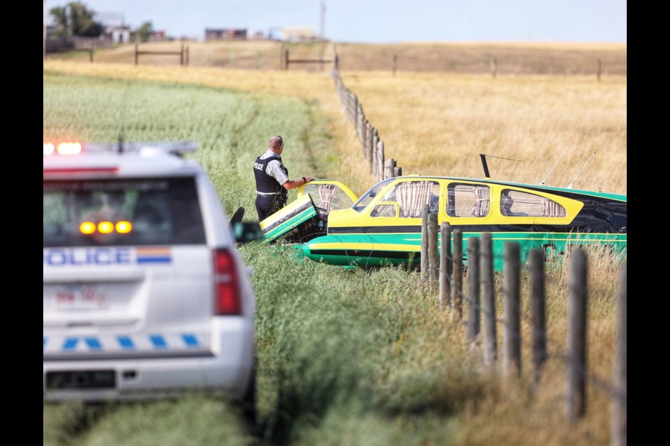 RCMP watch over a crashed Beechcraft Bonanza airplane in a field east of the High River Airport on August 10. Two occupants were transported hospital via ground ambulance, and the scene will be under investigation by Transport Canada.