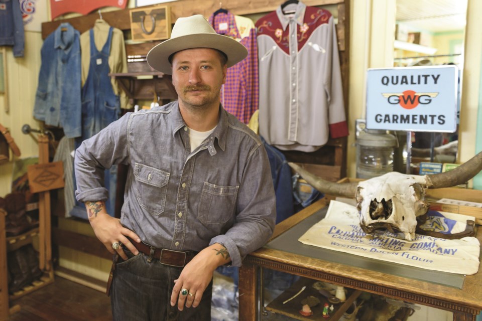 Cam Rooney, owner of Wild North Trading Co., leans on a display case with clothing hanging behind him at Bertie’s General Store in Diamond Valley on June 30. 