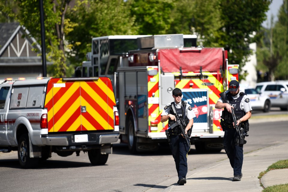 Heavily armed RCMP officers walk past emergency vehicles on Crystal Green Way during an incident in Okotoks on Aug. 15. 