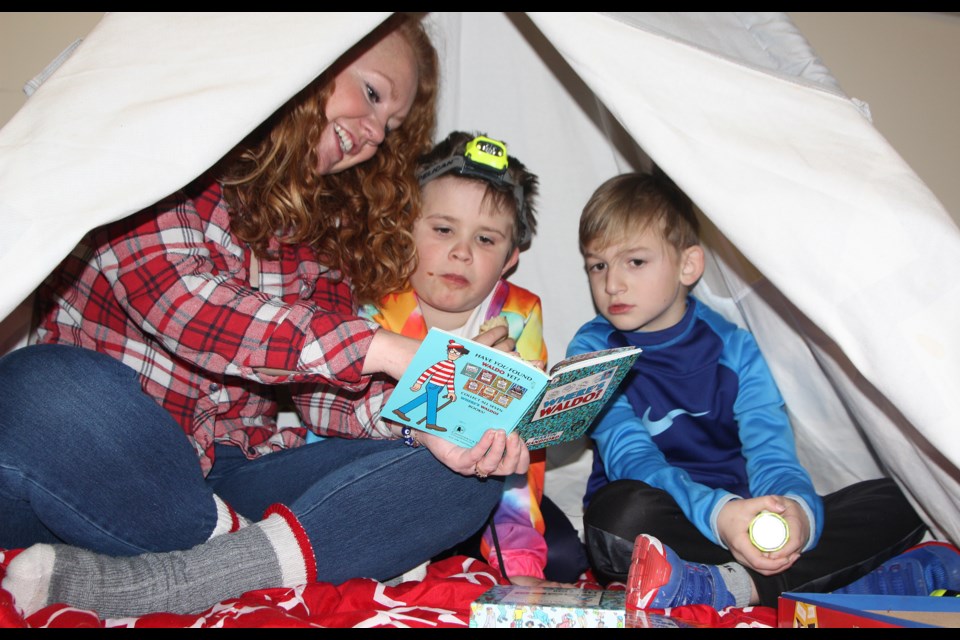 Nicole Privett reads a Where's Waldo book inside a cozy tent to son Jude, 8, and Taylem Beaudoin, 7, during Turner Valley School's Literacy Day on Jan. 27. (Tammy Rollie/Western Wheel)