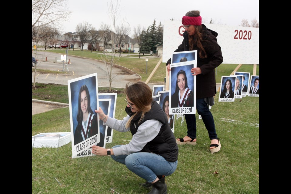 Foothills Composite High School counsellor Gina Kilbreath and vice-principal Kathryn Strilchuk put up some of the more than 400 portraits of grads placed along Cimarron Drive on May 4. (Bruce Campbell/Western Wheel)