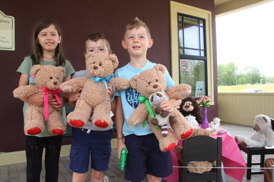 From left: Hayley, Carter and Connor Lamb with their matching teddy bears, which were given to them in memory of their late grandfather, outside the Okotoks Museum and Archives during the Teddy Bear Hunt on July 9. (Krista Conrad/Western Wheel)