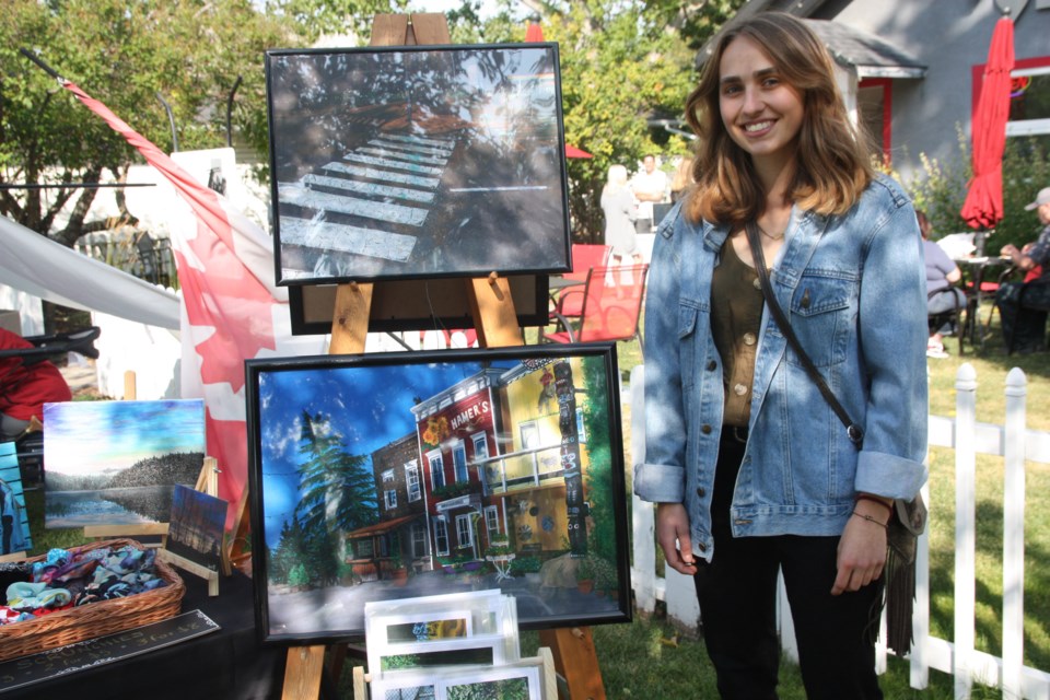 Okotoks artist Jessica Vidican with two of her acrylic paintings, top, the corner of N.Railway and 32 Street at night, and bottom, a scene from the Saskatoon Farm. Vidican was participating in the Okotoks ARTSWalk on Sept. 12. (Bruce Campbell, Western Wheel)