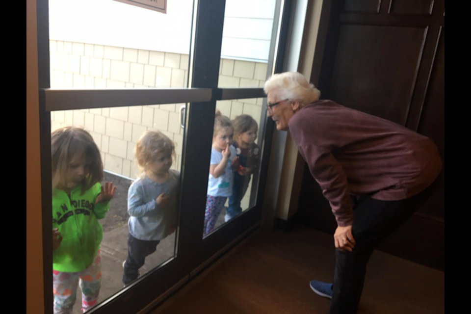 Tudor Manor resident Hillary McCullough says hello to VIK Academy daycare children in Okotoks. The residents and the students have been able to maintain their intergenerational connection despite the pandemic. (Photo submitted) 