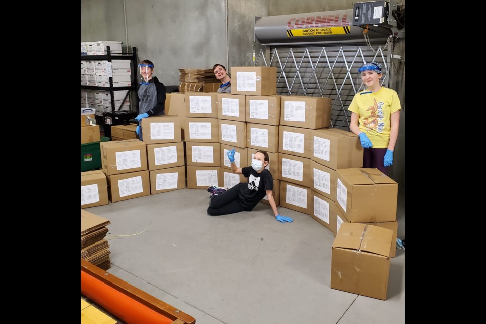 From left, Owen Plumb, Nicholas Plumb, Abigail Plumb and Emma Cunningham sit on boxes of approximately 600 face shields they helped make to give to those wanting COVID-19 protection. The four received The Town of Okotoks Leaders of Tomorrow Awards on April 15. (Photo submitted)
