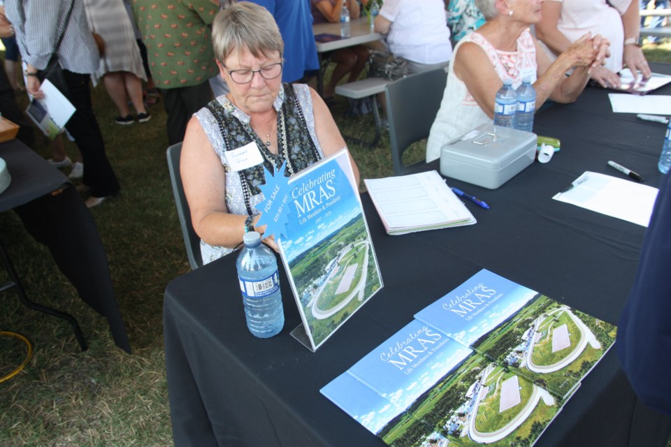 Suzanne Sills sells copies of Celebrating MRAS Life Members and Presidents 1907-2020 during the unveiling of the Legacy Wall on Aug. 13 at the Millarville Racetrack. (Bruce Campbell/Okotoks Today)