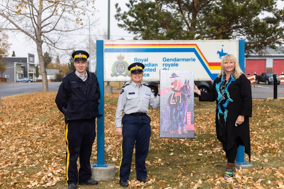 Artist Linda MacKay displays her painting with Turner Valley RCMP Sgt. Josh Atkinson and Staff Sgt. Laura Akitt that now hangs at the detachment.