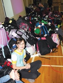 A John Paul II Collegiate student sits besides the more than 250 backpacks to be donated to families through the Foothills Magic of Christmas program.