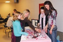 Behind the table from left, Joy-Lyn Stickel and Andrea Wilton-Clark attend to some potential jewelry buyers Feb. 6 at the Okotoks Recreation Centre. The pair are encouraging