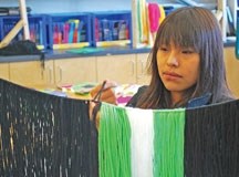 Sixteen-year-old Curdana Daniels ties knots using green, black and white yarn to create the fringe part of her grass dance outfit. The process is meticulous and