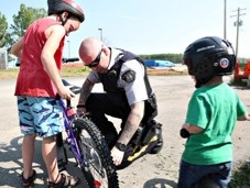 Turner Valley RCMP Const. Ken Moore fixes a chain on Jeffrey Wiens bike as his brother Kyler looks on. The two received a &#8216;ticket&#8217; for a free Freezie for wearing