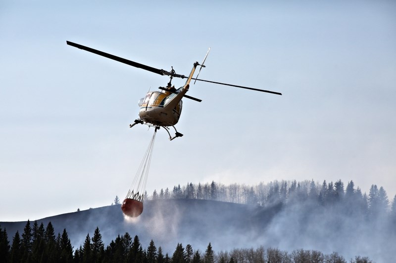 A helicopter carrying a load of water flies over a fire burning on the border between the MD of Foothills and Kananaskis on April 17.