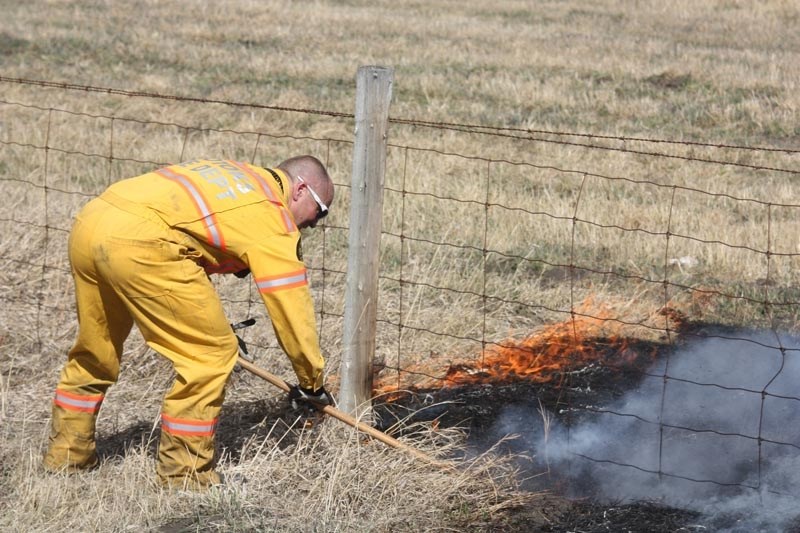 Okotoks firefighter Russ Friesen stomps out flames at a grassfire just east of the Okotoks overpass.