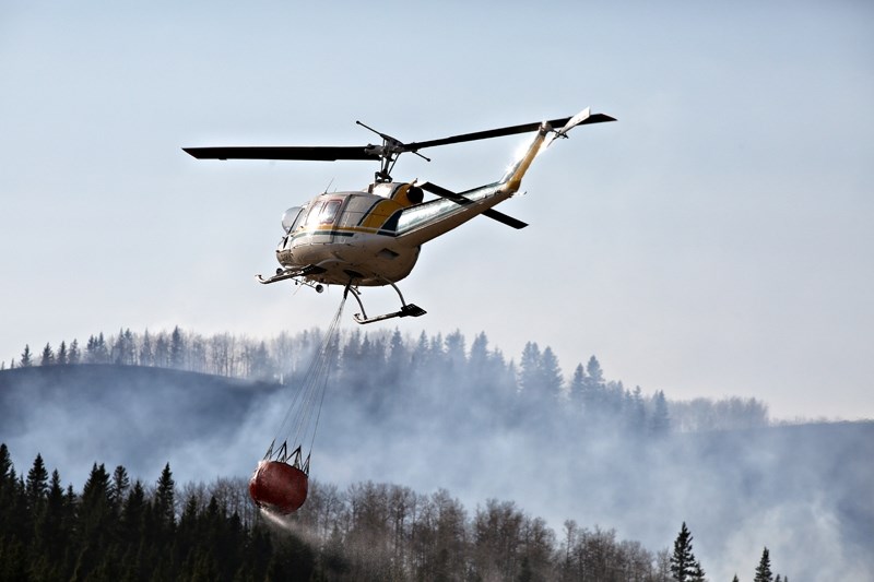 A helicopter carrying a load of water flies over a wild fire west of Secondary Highway 762 near the Kananaskis border as crews work to douse the flames spread by high winds