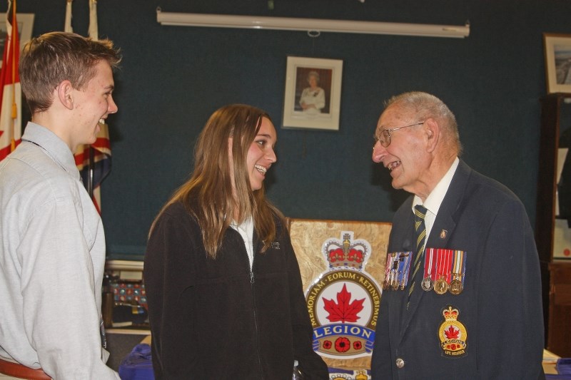Gordan Day, past president of the Royal Canadian Legion Turner Valley Branch #78, speaks with Edison School students Parker Antal and Melina Watson following the poster,