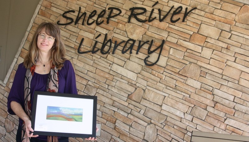 Former foothills resident Deb McPhee, who now lives in Calgary, holds one of the paintings she will have on display at the Sheep River Library&#8217; s gallery throughout