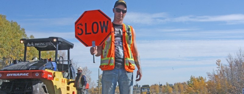Dustin MacAllister, a flagger with A&#038;A Paving, directs traffic at the intersection of Decalta Road and Main Street in Turner Valley on Oct. 2. Construction work on