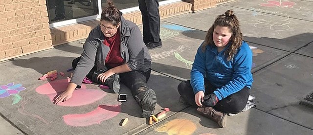 Ranger Bri McGuire, left, and Pathfinder Isabel Marchant decorate the sidewalk with flowers for the local unit&#8217;s World Association of Girl Guides and Girl Scouts
