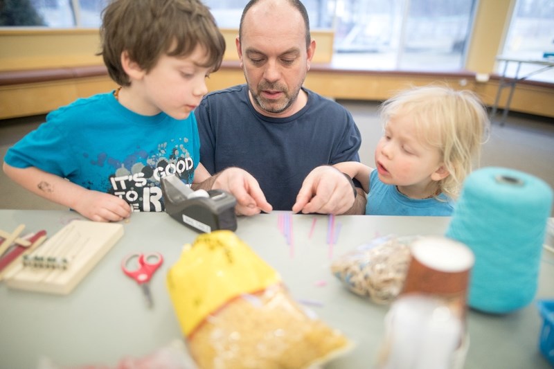 Mark Layton makes a pipe flute with his children Tyler, left, and Harrison at a Dad Project event at the Okotoks Public Library on March 30.