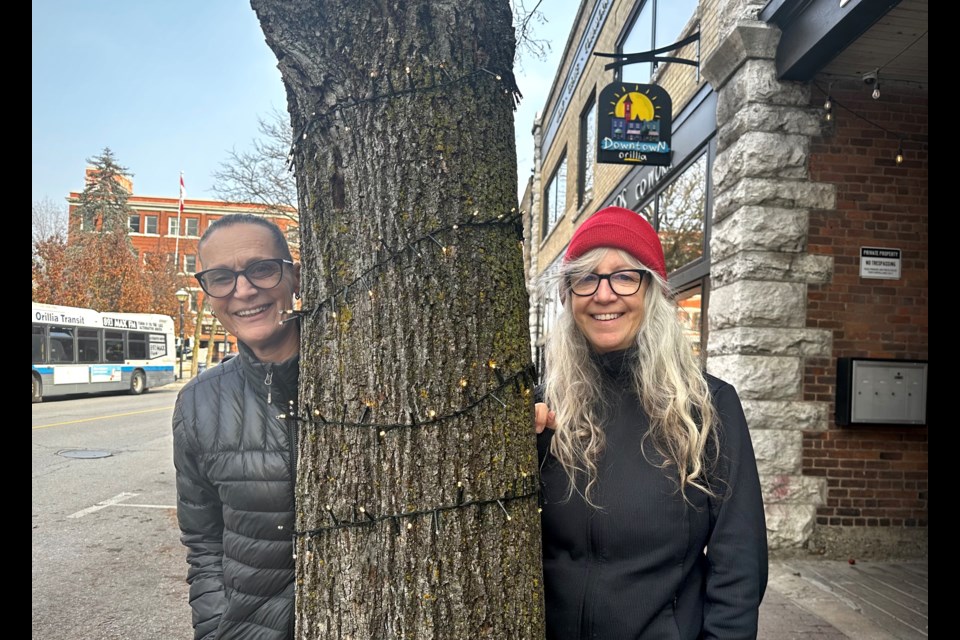 Anitta Hamming, left, and Leslie Fournier have organized campaigns in the wake of Orillia’s infamous Christmas tree lighting to help local non-profits. In the days since, Hamming has wrapped the trunks of the trees in front of Creative Nomad Studios in embrace of last week’s tree lighting. 