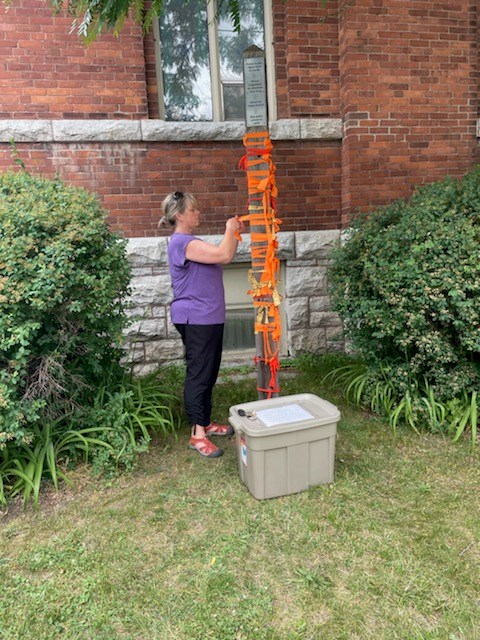 Beth Kudar ties an orange ribbon to the Peace Pole.