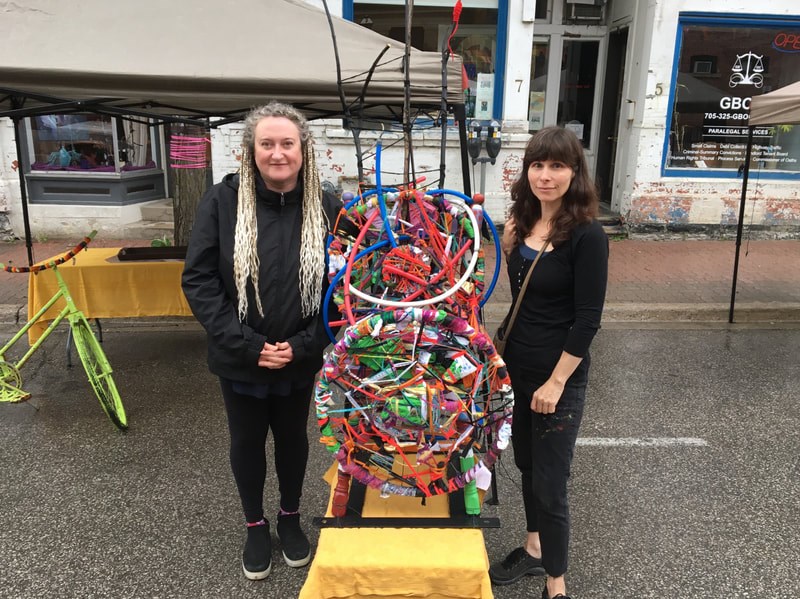 Local artists Sylvia Tesori and Patti Agapi in simpler times, with a collaborative piece in the Peter Street Arts District. credit Patti Agapi