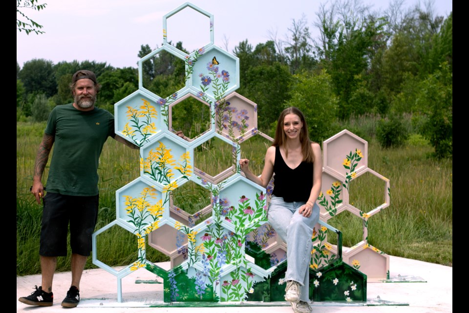Artist Rachel Babineau and metalwork artist Frank Ripley stand by the honey-combed shaped Wild Honey public art installation.