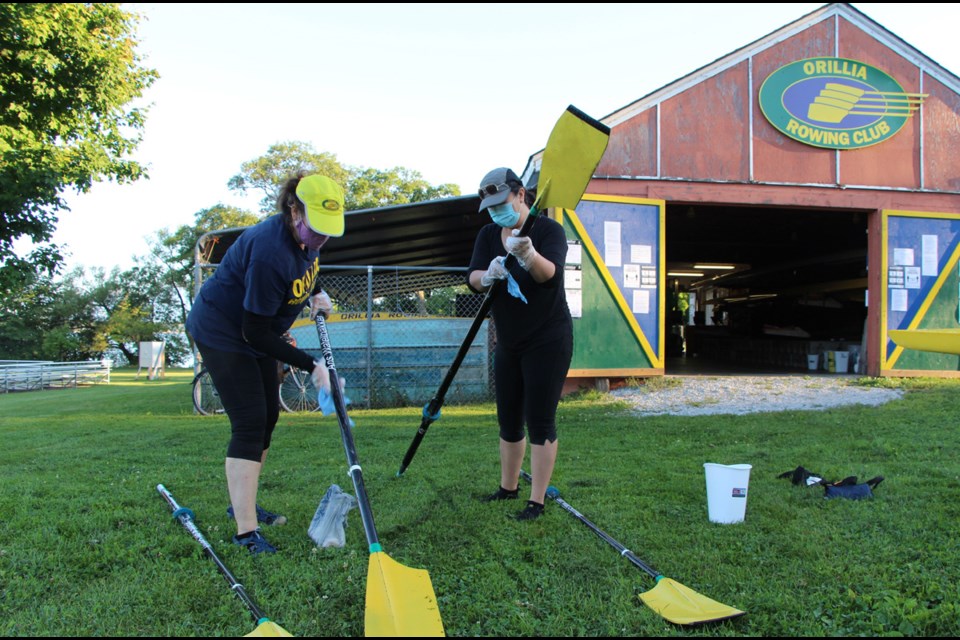 Orillia Rowing Club rowers Lorraine Manners, left, and Glo Cabugao clean and disinfect oars, as part of the Club’s COVID-19 safety guidelines. Kathy Hunt/OrilliaMatters File Photo