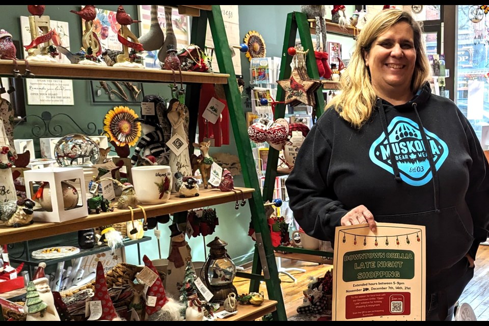 The Bird House Nature Company owner Patricia Cousineau displays a Downtown Orillia Late Night Shopping poster with QR code, in front of the Christmas display at her Mississaga Street store. Cousineau spearheaded the effort to get local downtown merchants to stay open late on Thursdays until Christmas. The initiative begins Thursday evening.