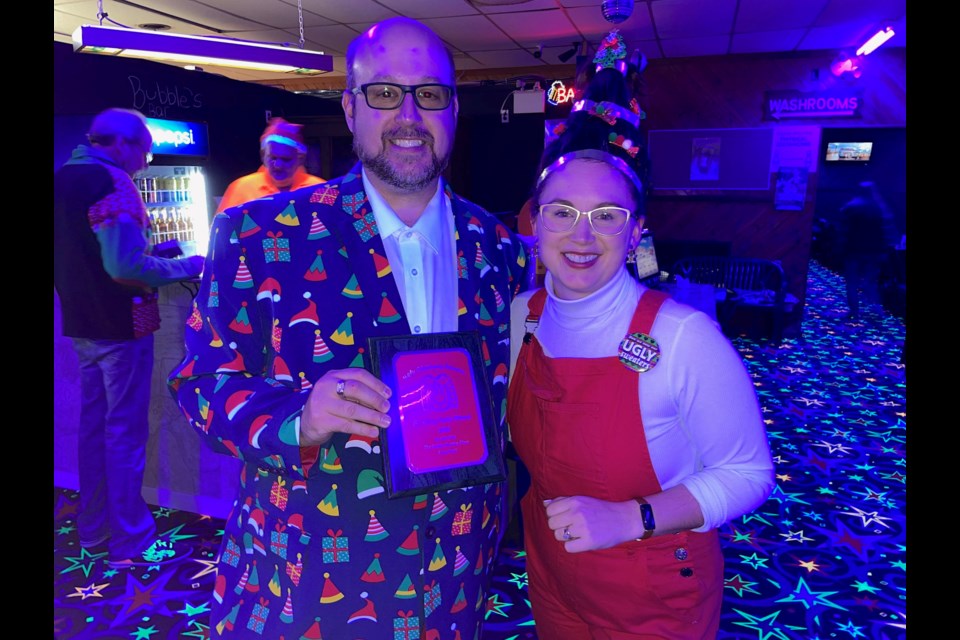 Derick Lehmann, organizer of the annual Ugly Sweater Bowling Party, presents a plaque to Katie Dewar for her Cindy Lou Who-inspired hair.