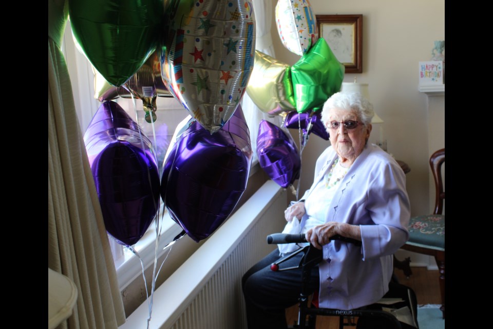 Sue Mulcahy sits at her living room window, surrounded by balloons, where she watched as a parade of well wishers drove by to help her celebrate her 100th birthday.