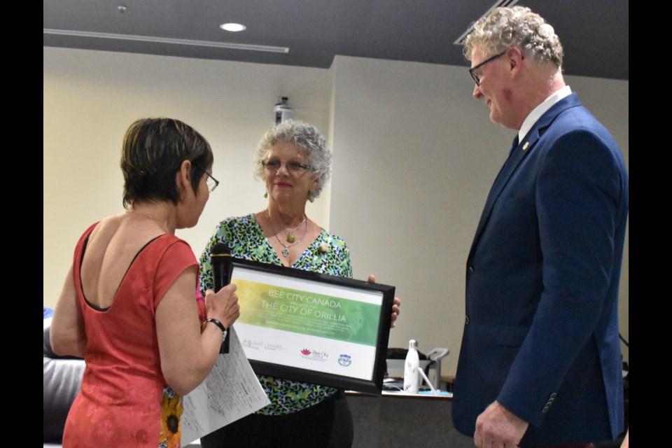 Jeannine Hutty, one of the key local advocates pushing for Orillia to become a Bee City, presents Mayor Steve Clarke with a certificate, while Shelly Candel, founder of Bee City, looks on. Dave Dawson/OrilliaMatters