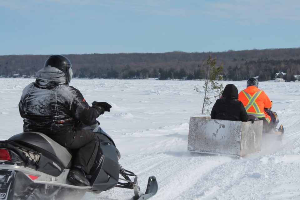 Residents of Christian Island cross the ice road on their snowmobiles.