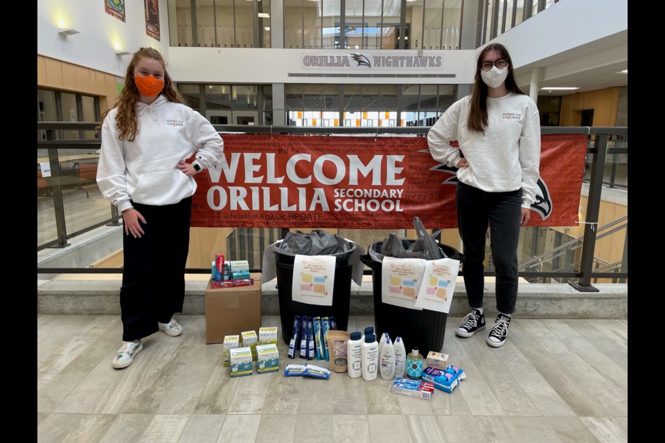 Chloe Bard and Sophia Armstrong in the Orillia Secondary School foyer next to a collection of donations for the Students for Change hygiene drive on June 22.