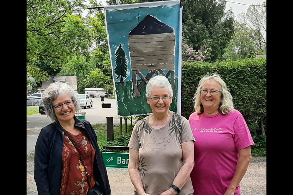 Hawkestone Hall 100th anniversary ad hoc committee members Marilyn Gregory, Joan Banbury and Tracey McKillop pose in front of one of the painted banners that can be found throughout the village in homage to the hall and its milestone. 