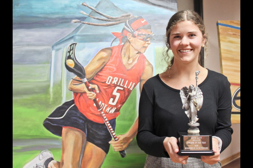 Annie Lloyd poses with the Orillia Athlete of the Year trophy she won Monday, in front of a painting of her by local artist Paul Baxter. Nathan Taylor/OrilliaMatters