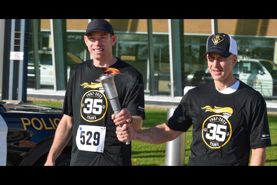 Stephan Graham, an Orillia athlete who competes for Special Olympics Ontario, left, accepts the torch alongside OPP Commissioner Thomas Carrique as the  35th annual Law Enforcement Torch Run for Special Olympics Ontario begins at OPP headquarters Sunday.