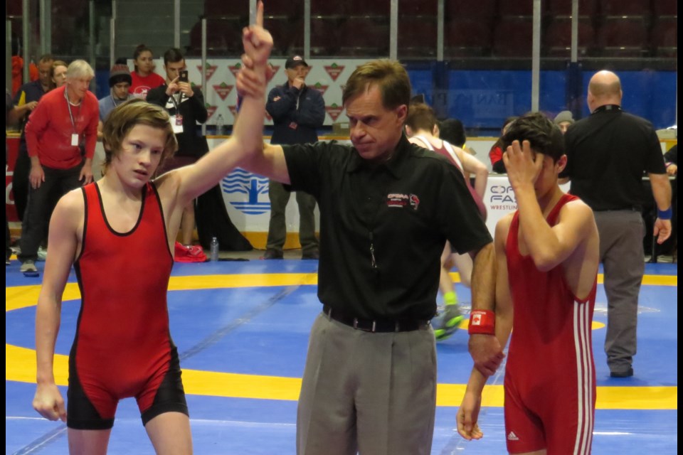Twin Lakes student athlete Dominic Ritchie has his arm raised in victory after defeating an opponent at the provincial high school wrestling championship.