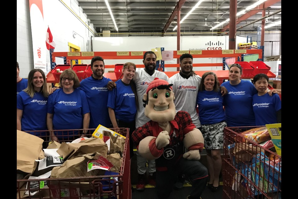 Defensive Lineman Jonathan Newsome and Linebacker Kevin Brown II (centre) posing with Ottawa Food Bank volunteers and the Redblacks mascot during the food sorting challenge.  Photo/ Brian Findlay