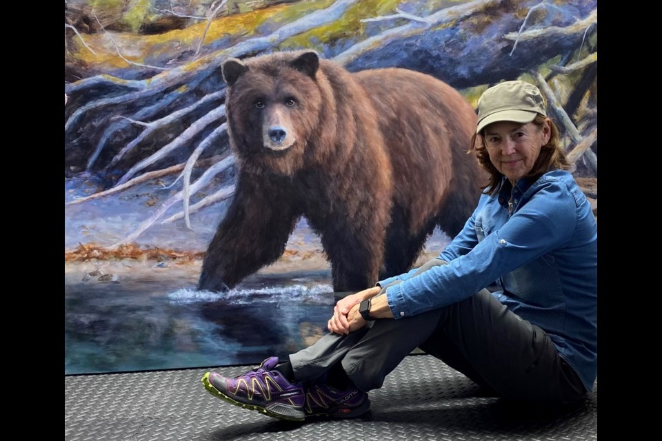 Whistler artist Doria Moodie sits next to one of her paintings.