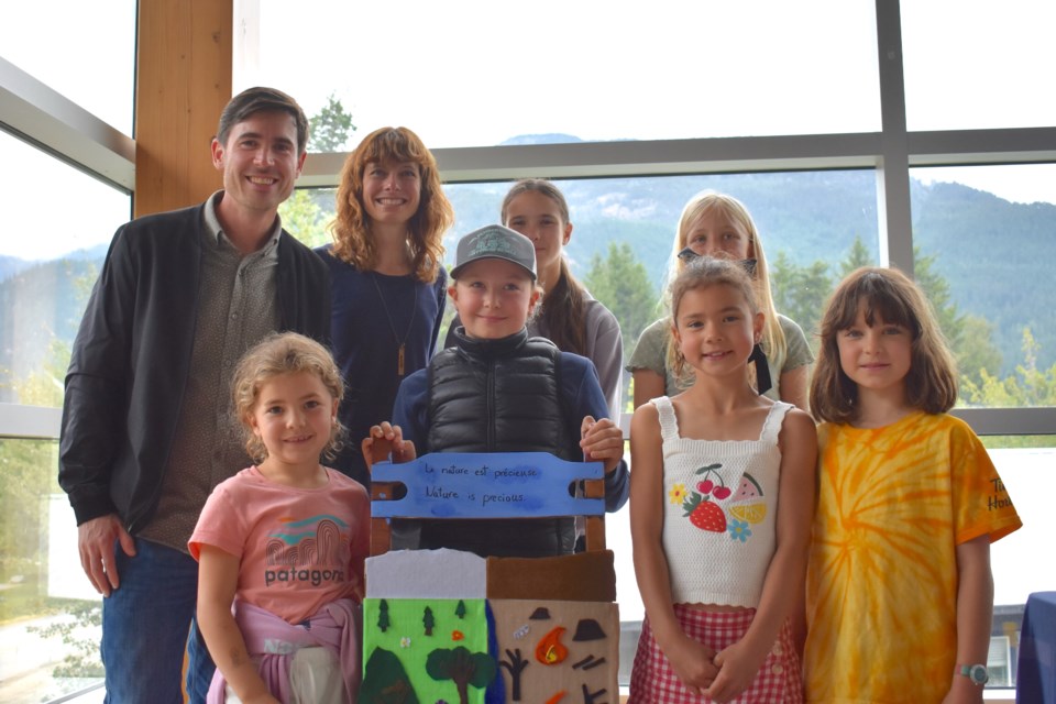 MP Weiler and Francophone school EA Carswell pose with the students behind the new Chair of the Next Generation. 